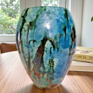 May include: A white ceramic mug with a black handle and the text "But First, Coffee" in a bold, black font. The mug is set against a blurred background, suggesting a cozy setting.