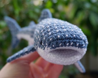 Może przedstawiać: Ręcznie robiony szydełkowy rekin wielorybi w odcieniach niebieskiego i białego. Amigurumi rekina ma teksturowany korpus z białymi kropkami, białą paszczę i szczegółowe płetwy. Ta miękka rzeźba to unikalny, ręcznie robiony przedmiot.