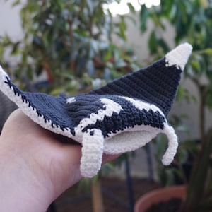 Op de afbeelding: Een handgemaakte gehaakte mantarog in marineblauw en wit. De rog heeft een witte buik en witte accenten op de vleugels. De vleugels zijn marineblauw met witte golfpatronen. Het haakwerk is gedetailleerd en het ontwerp is speels.