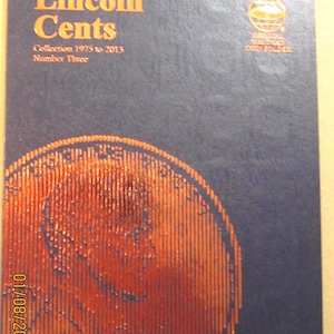May include: A dark blue coin folder titled "Lincoln Cents" with orange lettering and a large orange penny design. The folder is for a collection from 1975 to 2013. The words "Official Whitman Coin Folder" are also visible.