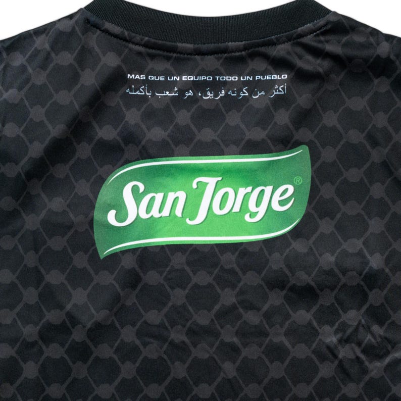 Puede incluir: Camiseta negra con un logotipo "San Jorge" verde y blanco en la espalda. La camiseta tiene un patr&oacute;n geom&eacute;trico en blanco y negro.