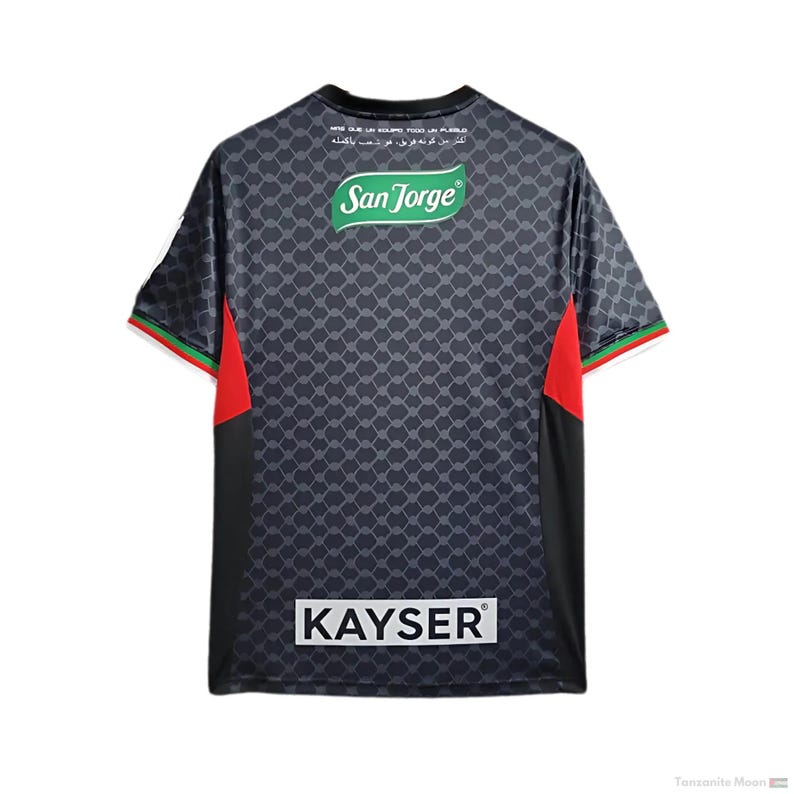 Puede incluir: Camiseta de f&uacute;tbol negra con detalles rojos y verdes. La camiseta tiene un patr&oacute;n de malla negro y gris y presenta el texto "San Jorge" y "KAYSER" en la espalda.