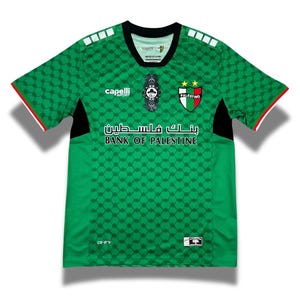 Puede incluir: Camiseta de fútbol verde con detalles en blanco y negro. La camiseta tiene un patrón geométrico y presenta el texto "Bank of Palestine" y el logotipo de la selección nacional de fútbol de Palestina.