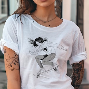 May include: White t-shirt with a black and white illustration of a woman skateboarding. The woman is wearing a hoodie and jeans. The illustration is on the front of the shirt.