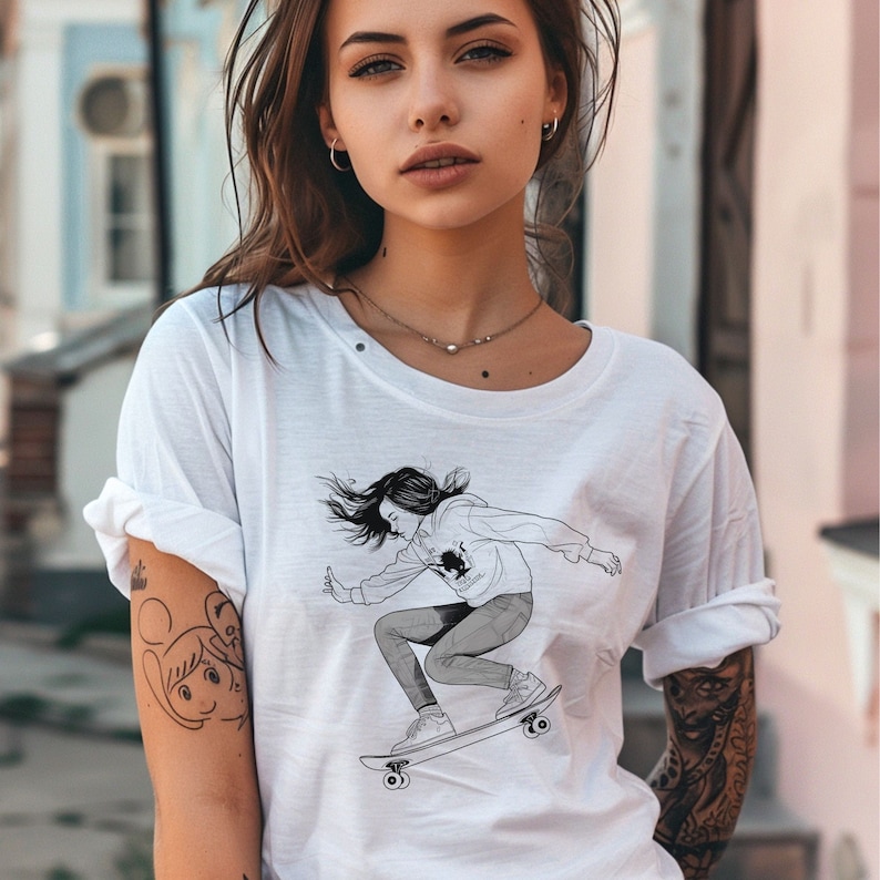 May include: White t-shirt with a black and white illustration of a woman skateboarding. The woman is wearing a hoodie and jeans. The illustration is on the front of the shirt.