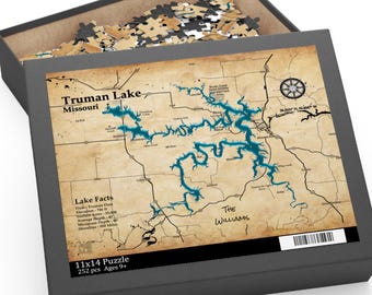 May include: A gray puzzle box with a map of Truman Lake, Missouri, in blue and brown tones. The box is open, revealing puzzle pieces. Text on the box includes "Truman Lake Missouri," "Lake Facts," and "11x14 Puzzle 252 pcs Ages 9+".