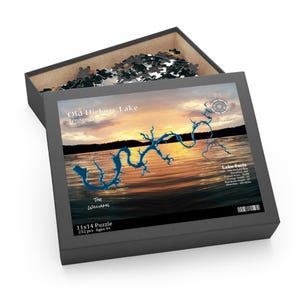 May include: A 252-piece puzzle in a black box, featuring a sunset over Old Hickory Lake in Tennessee. The puzzle image includes a blue outline of the lake and text that reads "The Williams" and "Lake Facts". The box is 11x14 inches.