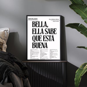 Op de afbeelding: Zwart-witte ingelijste print met de tekst "BELLA, ELLA SABE QUE ESTA BUENA" en songteksten van het nummer "Ella Baila Sola" van Peso Pluma. De print hangt aan een zwarte muur met een zwart nachtkastje en een groene plant.