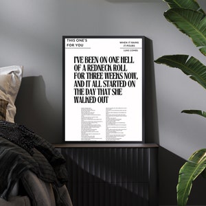Op de afbeelding: Zwart-witte afdruk van songteksten van Luke Combs. De tekst is voor het nummer "When It Rains It Pours". De afdruk is ingelijst en hangt aan een muur in een slaapkamer.