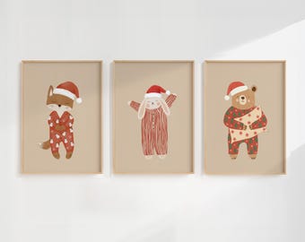 May include: Three framed prints featuring festive animal illustrations. A fox, bunny, and bear are depicted in red pajamas and Santa hats. The fox and bear are holding gifts. The prints have a neutral background and gold frames.