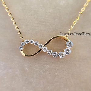 Pode incluir: Colar com pingente de infinito dourado com corrente. O símbolo do infinito é cravejado com pedras preciosas redondas e transparentes. O texto "LustaraJewellers" é visível na imagem.