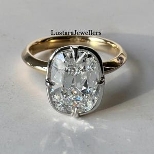 Peut inclure: Une bague en or et argent avec une grosse pierre précieuse transparente de taille coussin. La bague a un anneau en or et un sertissage en argent autour de la pierre précieuse. Le texte "LustaraJewellers" est visible.