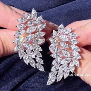 May include: A pair of dazzling, leaf-shaped earrings. Each earring features multiple marquise-cut, clear gemstones set in a silver or white metal. The gemstones are arranged to mimic the shape of a leaf, creating a sparkling, elegant design.