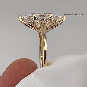 Op de afbeelding: Een gouden ring met een grote, heldere edelsteen in marquise-slijpvorm, gezet in een decoratieve zetting met organische, takachtige pootjes. De ringband is van glad, gepolijst goud. De tekst LustaraJewellers is rechtsboven zichtbaar.