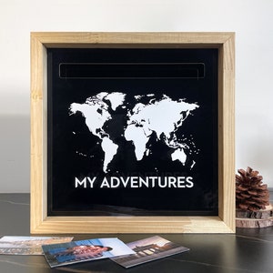 May include: A wooden shadow box with a black background featuring a white outline of a world map and the text "MY ADVENTURES". The box is open and there are three photos inside.