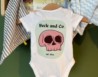 Ropa infantil única Beck and Co. Skull Baby Design disponible como mono o camiseta para bebé, colores personalizables, desde recién nacido hasta los 5 años