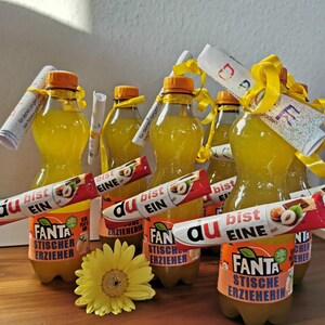 K&ouml;nnte beinhalten: Sechs Glasflaschen mit orangenlimonade mit gelben Etiketten, auf denen "Fanta" und "Stischer Erzieher" oder "Stische Erzieherin" steht. Jede Flasche hat ein gelbes Band um den Hals gebunden und ein zusammengerolltes Papier mit Text. Eine gelbe Sonnenblume befindet sich im Vordergrund.