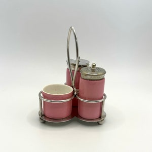 May include: A silver condiment set with three pink ceramic containers. The set has a handle and sits on a silver stand.