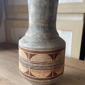 Może przedstawiać: Szary ceramiczny wazon z geometrycznym wzorem brązowych i beżowych kół. Wazon ma fakturowaną powierzchnię i szeroką podstawę.