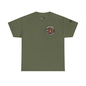 May include: Olive green t-shirt with a circular patch on the chest. The patch features text that reads "Charlie Company" and a design with a cross, a figure, and the American flag. A small flag design is on the right sleeve.