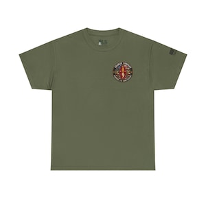 Könnte beinhalten: Olivgrünes T-Shirt mit einem kreisförmigen Aufdruck auf der Brust mit der Aufschrift "Charlie Company". Das Design zeigt ein zentrales Design mit einer rot-weißen Figur, umgeben von Text und anderen Elementen. Auf dem rechten Ärmel befindet sich eine kleine Flagge.