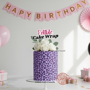 May include: A cylindrical cake featuring a purple leopard print pattern, adorned with white roses and foliage. The cake is decorated with a "Happy Birthday" banner and a "Edible Cake Wrap" cake topper.