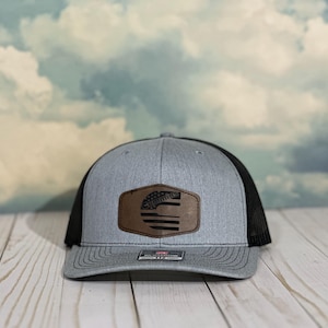 May include: A gray and black trucker hat with a brown leather patch featuring a stylized American flag and the word "United".