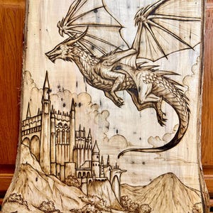 May include: A wood-burned image of a dragon flying over a castle. The dragon is detailed with scales and wings. The castle is a medieval style with towers and a gate.