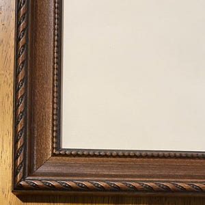 May include: A rectangular picture frame with a dark brown wood finish and a textured rope-like pattern along the outer edge. The frame features a mitered corner joint and a smooth inner border, surrounding a plain, light cream-colored mat board.