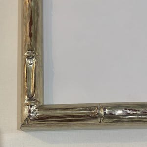 May include: A silver-colored picture frame with a bamboo-style design. The frame has a textured surface and a light, metallic sheen. The corners are mitered, and the overall design is simple and elegant.