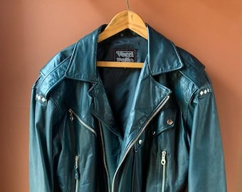 May include: A dark blue leather motorcycle jacket with a zipper closure, a belt at the waist, and silver studs on the shoulders. The jacket has a label that reads "Vern Pelle".