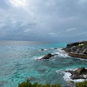 May include: A rocky coastline with turquoise water crashing against the shore. The sky is overcast with gray clouds.