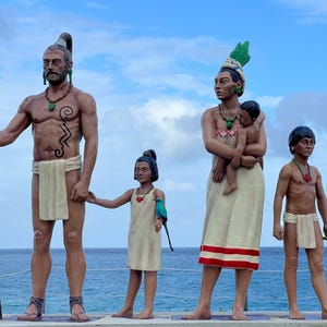 May include: A family of four statues depicting indigenous people. The father holds a spear, the mother holds a child, and the two children stand beside them. The statues are painted in earthy tones and have intricate details.
