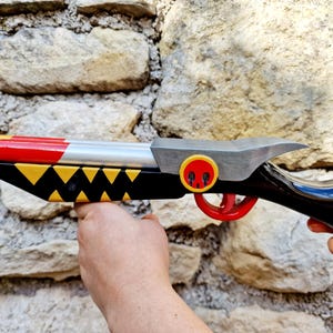 Puede incluir: Una pistola de juguete colorida con un diseño amarillo, rojo, plateado y negro. El cañón es amarillo y rojo, con un cuerpo plateado. El mango es negro con detalles amarillos y un gatillo rojo. Tiene un emblema de calavera.