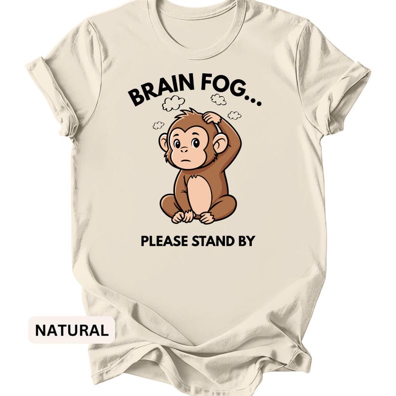 Puede incluir: Camiseta color crema con el texto "BRAIN FOG... PLEASE STAND BY" y un dibujo de un mono. El mono marr&oacute;n parece confundido y se agarra la cabeza. La palabra "NATURAL" est&aacute; impresa en la parte inferior.