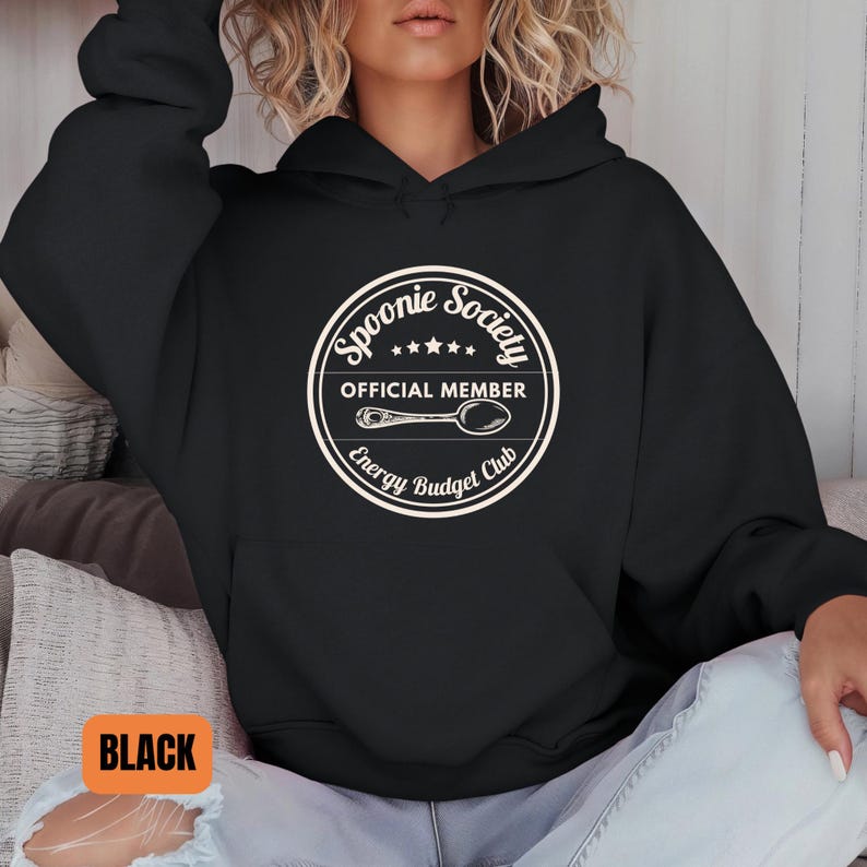 May include: Black hoodie with a white circular graphic that reads "Spoonie Society Official Member Energy Budget Club" with a spoon illustration. The word "BLACK" is in an orange rectangle at the bottom left.