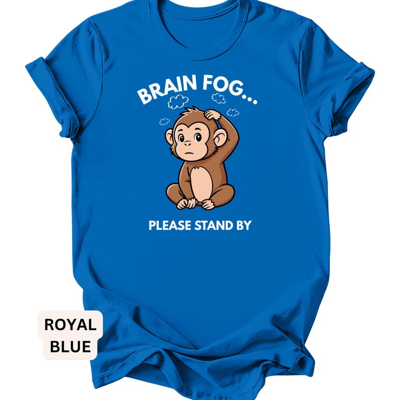 Puede incluir: Camiseta azul real con el texto "BRAIN FOG... PLEASE STAND BY". La camiseta presenta un mono de dibujos animados con una mano en la cabeza, rodeado de gr&aacute;ficos de nubes. La camiseta es de color azul real liso.