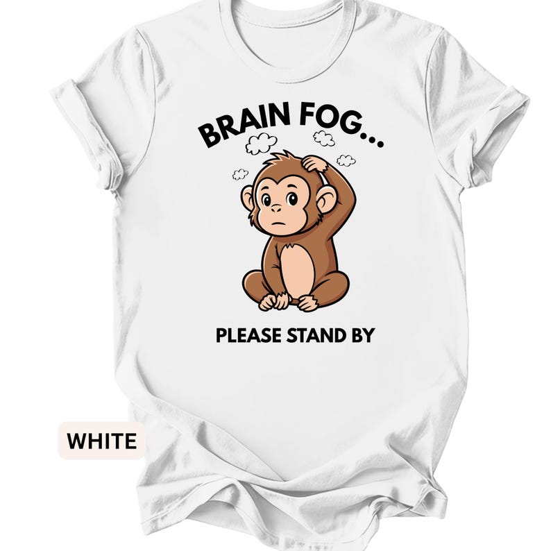 Puede incluir: Camiseta blanca con un dise&ntilde;o de mono de dibujos animados. El mono marr&oacute;n est&aacute; sentado, con la mano en la cabeza. El texto encima del mono dice "BRAIN FOG..." y debajo, "PLEASE STAND BY".