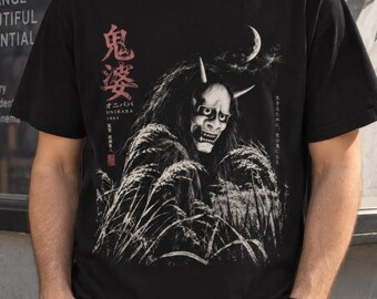 May include: A black short-sleeve t-shirt featuring a white graphic print of a horned demon mask emerging from tall grass under a crescent moon. The design includes red Japanese kanji characters and the text "ONIBABA 1964" in white lettering.