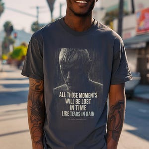 Könnte beinhalten: Dunkelgraues T-Shirt mit einem Graustufenbild einer Person im Regen. Der Text "ALL THOSE MOMENTS WILL BE LOST IN TIME LIKE TEARS IN RAIN" ist unter dem Bild aufgedruckt. Ein lässiges Kleidungsstück.