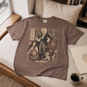 May include: A brown short-sleeve t-shirt featuring a graphic print of characters from the film Labyrinth. The design includes Jareth, Sarah, Hoggle, Ludo, and Ambrosius with Japanese text and the year 1980 printed in a muted, vintage-style color palette.