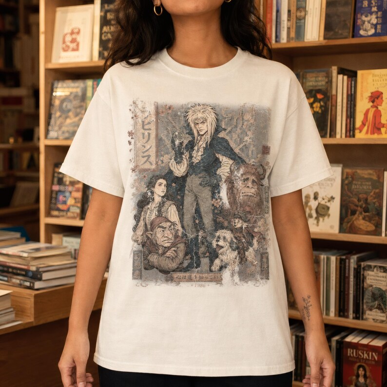 A woman wears an olive green t-shirt with a graphic of Jareth the Goblin King, Sarah, Hoggle, Ludo, and Sir Didymus in a Japanese poster art style, with Japanese text on the left.