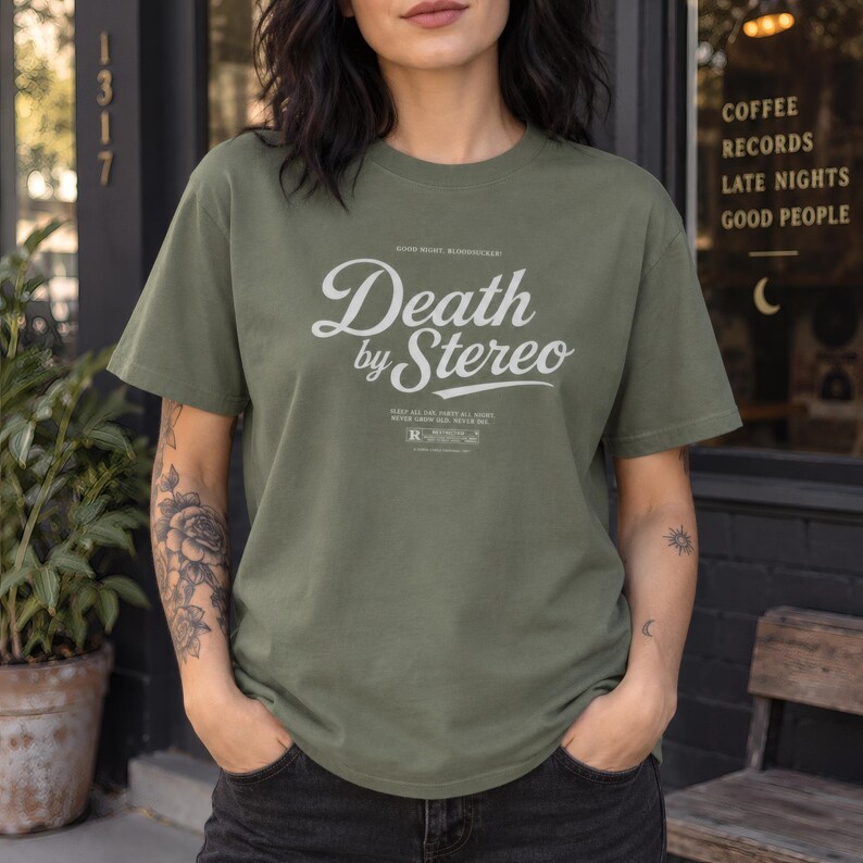 A person wearing a muted green crewneck t-shirt with white Death by Stereo graphic lettering.