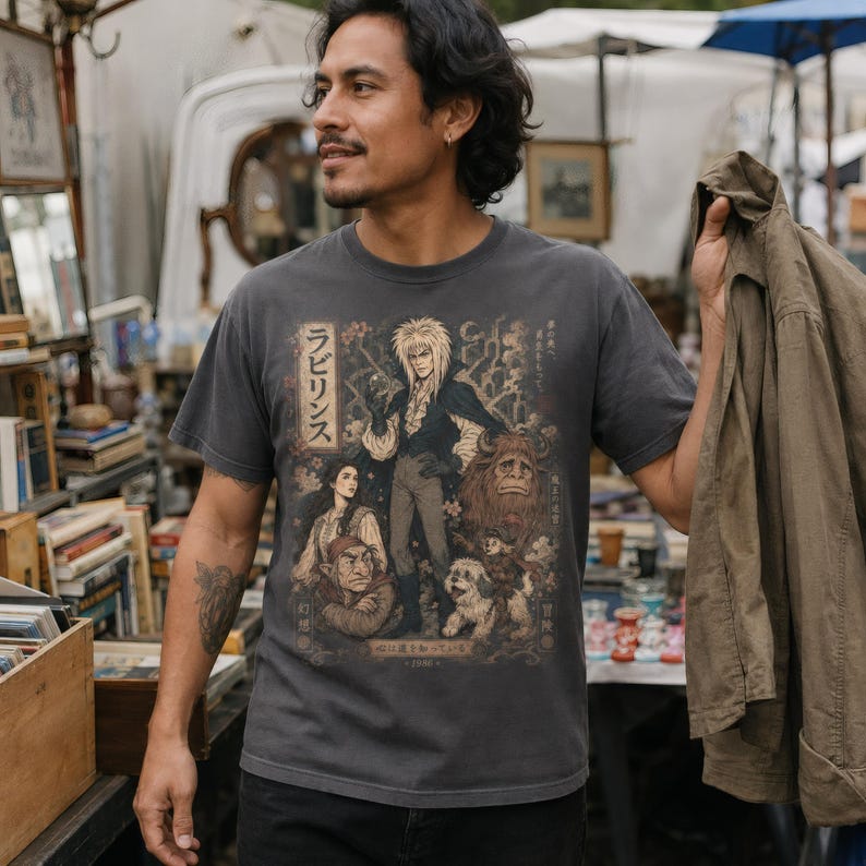 A woman wears a dark gray t-shirt with a graphic of Jareth the Goblin King, Sarah, Hoggle, Ludo, and Sir Didymus in a Japanese poster art style, with Japanese text on the left.