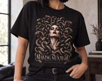May include: A black t-shirt featuring a graphic print of a person with snakes for hair, resembling Medusa. The text "MAKING MEN HARD" is printed in a stylized font below the image, followed by the smaller text "One look is all it takes."