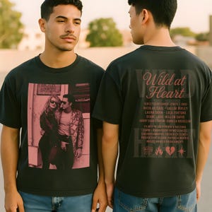 Puede incluir: Camisetas gris oscuro con una imagen rosa de la película "Wild at Heart". La parte delantera muestra una pareja frente a un edificio con el texto "HOTEL BRAZIL". La parte trasera tiene el título y los créditos de la película en rosa.