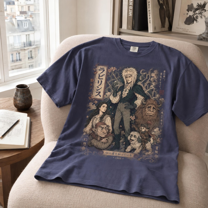 May include: A slate blue short-sleeve t-shirt featuring a detailed graphic print of characters from the film Labyrinth, including Jareth, Sarah, Hoggle, Ludo, and Sir Didymus, with Japanese text and cherry blossom accents integrated into the design.