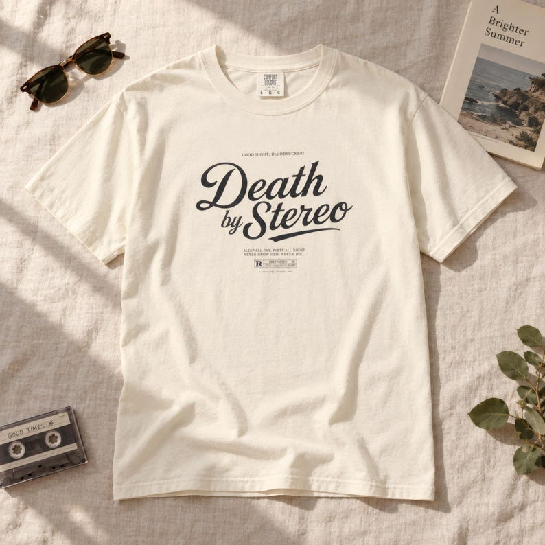 An off-white or cream t-shirt with black Death by Stereo lettering laid flat on neutral fabric.