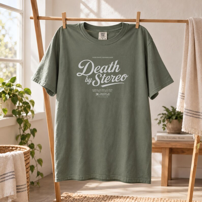 The same muted green t-shirt with Death by Stereo text hanging on a wooden clothing rack.