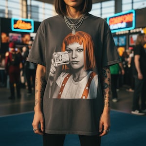 May include: Dark gray t-shirt featuring a graphic of a woman with orange hair holding a "MULTIPASS" ID card. The shirt has a vintage look and is part of a pop culture collection.